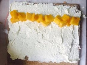 奶油加糖打好，抹到蛋糕上面，放上芒果。用擀面杖在后面推动，把它卷成卷，放在冰箱冷藏30分钟。取出切块。