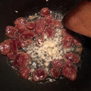 炒至腊肠表面微焦，下入蒜末煸出香味。