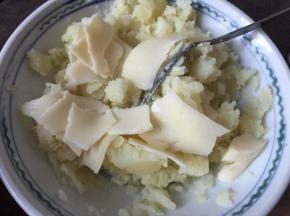 将蒸熟的土豆去皮趁热加入奶酪用汤匙压成泥