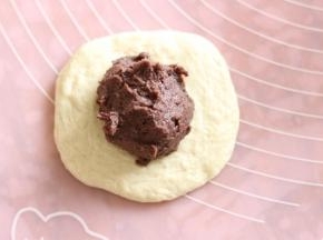 取一个面团，按扁包入豆沙馅。