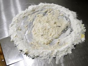 将周围的面粉向中间勾入混合，混合到中间不流动时，用刮板收起周围材料，混合按压