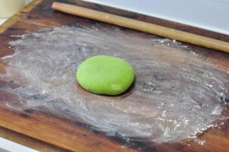 案板上撒上玉米面面扑，将面团揉圆，再用手掌压一压，压扁。