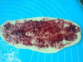 取一个松弛好的面团，擀成椭圆形，刷上蓝莓果酱，