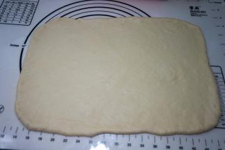 面团从桶中取出，放在揉面垫上，排气揉圆，盖保鲜膜松弛10分钟，然后擀成长40厘米、宽30厘米左右的长方形面片，厚约6、7毫米