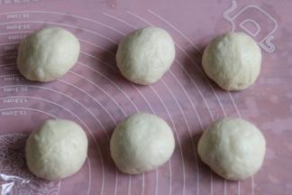 6取出发酵好的面团，挤压排气，然后整个面团称重，平均分成六等份，每个小面团都要用手滚圆，然后保鲜膜覆盖松弛（根据气温，温度25度以下松弛20分钟）15分钟。