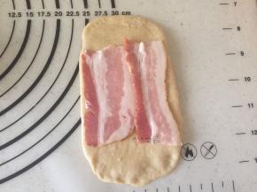 松弛好的面团擀成长的面片，上面码上2片培根