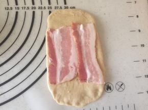 松弛好的面团擀成长的面片，上面码上2片培根