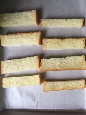 切好的吐司条摆放在铺了油纸的烤盘上，烤箱预热170度预热