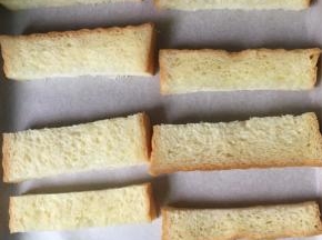 切好的吐司条摆放在铺了油纸的烤盘上，烤箱预热170度预热