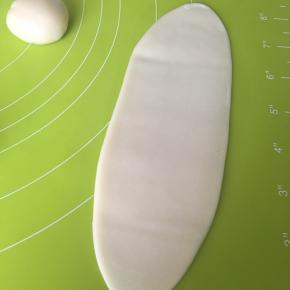 从后面像包包子一样收口，然后翻面收口向下，用不粘擀面杖擀成牛舌状