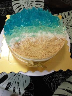 然后挨着浅蓝色的酒冻铺上饼干碎，最后在酒冻和饼干碎之间撒上椰丝，充当浪花。