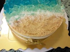 然后挨着浅蓝色的酒冻铺上饼干碎，最后在酒冻和饼干碎之间撒上椰丝，充当浪花。