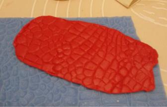 准备一片硅胶的鳄鱼纹模，红色干佩斯擀平后放在鳄鱼纹模上，用擀面杖轻压出纹理