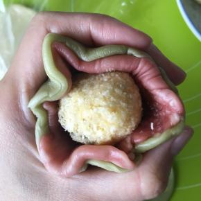 把两份不同颜色的面皮叠在一起，包入冷藏之后的椰蓉馅，收口，捏紧