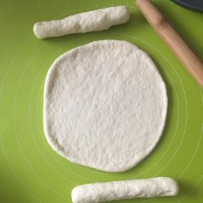 面团分别为两份，一份擀成9寸圆形大小，两根火腿肠用另一份面团擀长包起来