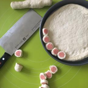 9寸面皮放入抹了一层油的披萨盘里，抱着火腿肠的面团用锋利的刀切片，摆放在披萨边上，烤箱预热180度，上下热风循环火