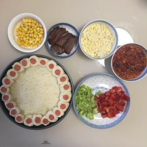 取出披萨，玉米剥粒煮熟，腊肉切片，青椒和红椒洗净沥干水切丁