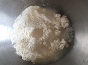面桶内倒入高筋面粉，中间挖小孔，倒入活性干酵母，盐和糖对角线放置，倒入清水