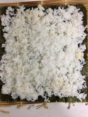 将稍微有温度的米饭均匀的铺在紫菜上面