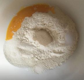 大碗内倒入高筋面粉，中间挖一小孔小孔内倒入酵母，白砂糖和盐对角线放，倒入10g全蛋液