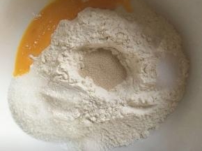 大碗内倒入高筋面粉，中间挖一小孔小孔内倒入酵母，白砂糖和盐对角线放，倒入10g全蛋液