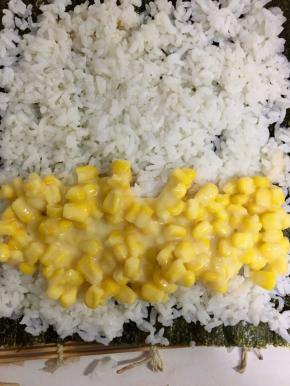 将混合好的炼乳玉米粒铺在米饭的下端，开始卷起的地方