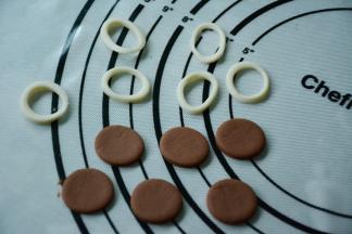 选择大小不一的裱花嘴分别在白色饼干团和巧克力饼干面团上压出不同大小的圆。白色饼干圆圈压好之后再用小一号的裱花嘴压出小一号的小圆圈，这样方便后面露出眼睛黑色部分。