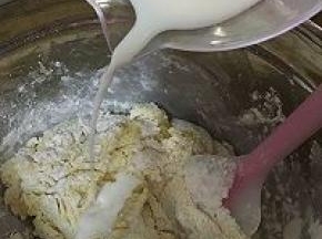 随后，倒入一半的牛奶，使用拌刀翻拌。按照干粉——牛奶——干粉的步骤，将干粉和牛奶拌入盆中，不要过度搅拌，直到没有干粉即可。