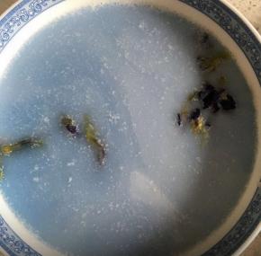 把泡好的糯米的水倒掉，加入100ml的椰浆和蝶豆花水，混合，挑出蝶豆花，煮饭键煮上