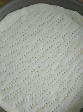 发酵好的面团取出揉搓排气，分成两份（这个材料是两个披萨饼胚的量8寸）取其中一份擀成比披萨盘稍微大点的圆形用叉子叉出小洞（这样做防止在烤的过程中鼓包）放入披萨盘里
