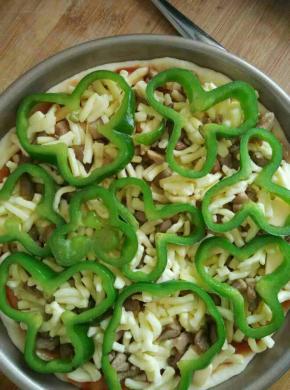 抹上披萨酱，撒上一层奶酪，铺上鸡丁肉，再撒上一层奶酪，上面铺上青椒圈
