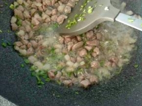 5、倒入瘦肉丁翻炒，中途加入葱姜一起炒。
