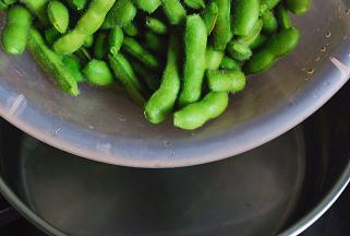 锅中水烧开，倒入剪好的毛豆，倒入几滴色拉油，煮至7 分熟捞起