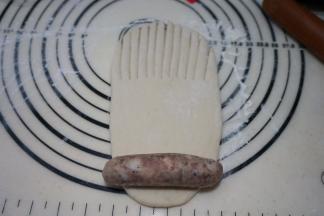 取一个面团擀成长方形，上半截1/2或者1/3处用刀切成梳子齿状，将一根香肠码放在最下面