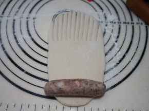 取一个面团擀成长方形，上半截1/2或者1/3处用刀切成梳子齿状，将一根香肠码放在最下面
