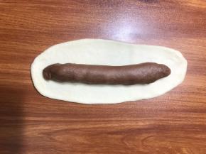 再取白色面团按扁排气，擀至长条，包裹刚才的面团条。