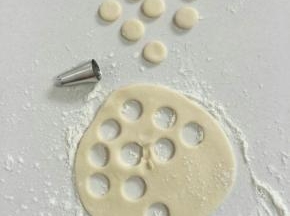 取一个白色小剂子揉圆后，撒少许面粉，用手按扁，再用裱花嘴按压出10个小圆，其中5个用来做猪猪包的鼻子，5个用来制作猪猪包的耳朵！（红色的面团也用同样的办法。）

