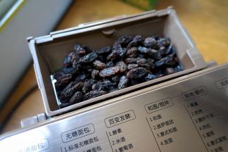葡萄干入面包机的果料盒中，过程中会自动打开盖子将葡萄干落入桶中；