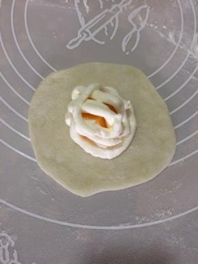 冷藏后的面团分成30克一个，沾手粉搓圆擀成圆皮，在粉皮中心挤一圈奶油，放上芒果粒，再挤一圈奶油