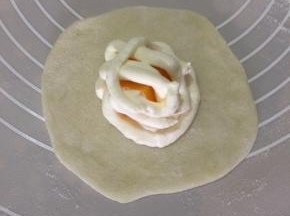 冷藏后的面团分成30克一个，沾手粉搓圆擀成圆皮，在粉皮中心挤一圈奶油，放上芒果粒，再挤一圈奶油