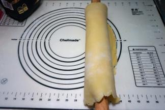 用擀面杖将面皮卷起来，这样面皮不会断裂；