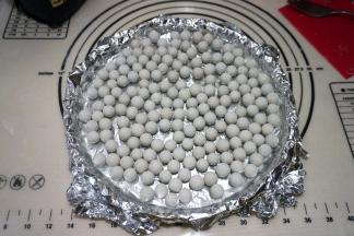 上铺锡纸，与面皮贴合，将烘焙石子撒在上面，如果没有烘焙石可以用干豆子或者锡纸包的石头放在上面代替；