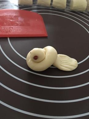 再像平常打结一样，给面条打个结，稍微整形一下！在头部那里捏出一个小尖嘴巴！用红豆代替小鸟的眼睛！尾巴部分用手掌压扁，用刀背或者用刮板压出纹理！