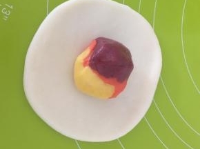 取一个水油皮压扁擀成饺子形状，包入一个油酥