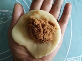 取一个面团，两套捏紧，放手心里按压扁；包入红糖