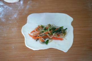 取其中的一个小剂子，将抹油的一面朝向案板，用擀面杖将其擀成薄薄的面皮，圆的长的不规则形状的都成；用筷子夹取适量的馅料放在靠近下面的面皮处