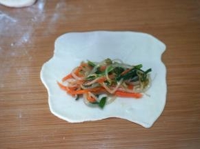 取其中的一个小剂子，将抹油的一面朝向案板，用擀面杖将其擀成薄薄的面皮，圆的长的不规则形状的都成；用筷子夹取适量的馅料放在靠近下面的面皮处