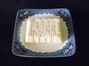 把豆腐盒正面朝上，撕去塑料包装薄膜，把盘子扣在豆腐盒上，再把盘子翻过来，豆腐的包装盒很轻松的就能拿下来。