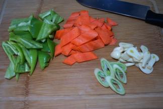 尖椒去蒂去籽切块，胡萝卜用半根切象眼片，大葱斜切成丝，大蒜切片
