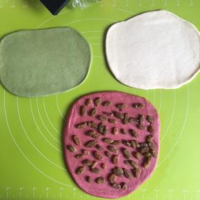 取出面团每一份都擀扁仔细排出气体，葡萄干提前用清水泡一下，沥干水，把葡萄干铺匀在红色面团上